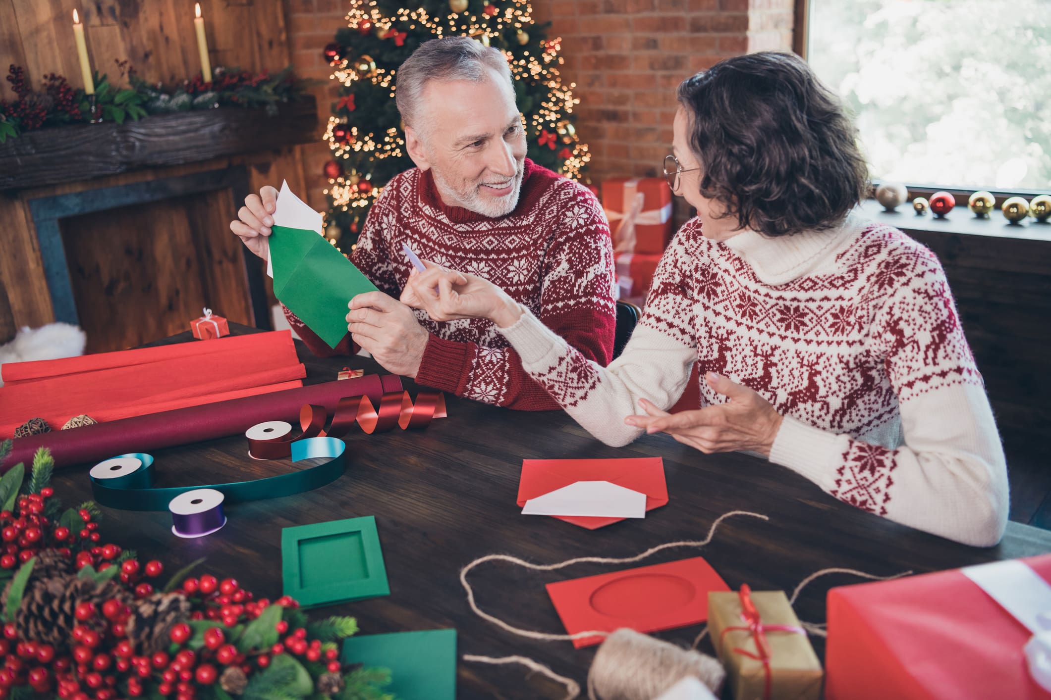 Photo of glad positive couple grandma talk grandpa packing envelop letter wear ornament sweater home indoors Photo of happy positive couple talking, grandma and grandpa while packing envelop letter wearing ornament sweaters home indoors